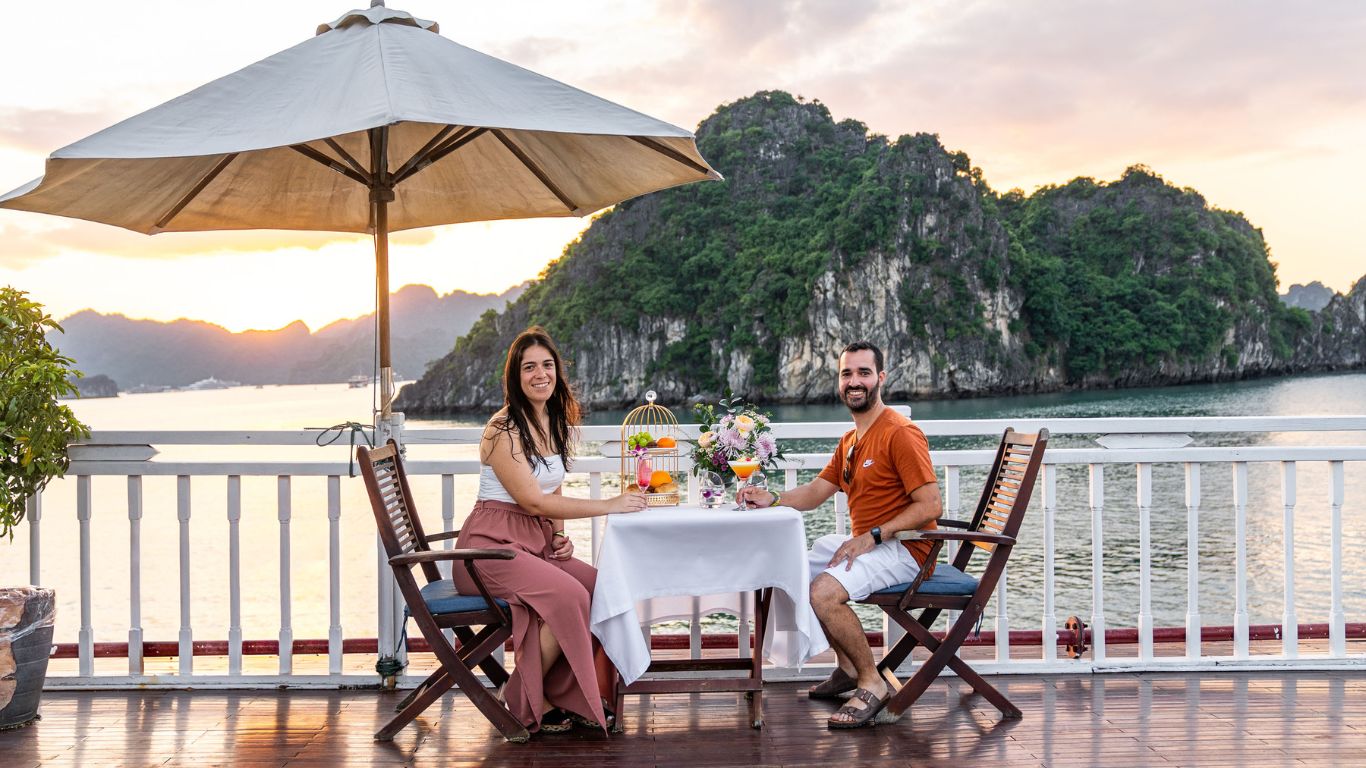 Travelers having dinner on a cruise balcony overlooking limestone islands at sunset in Halong Bay, Vietnam.