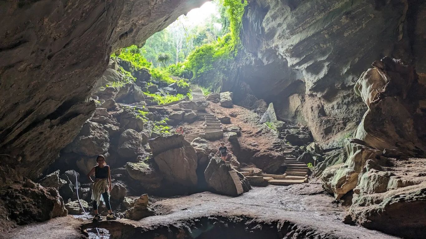 Visitors exploring the rocky interior of the Cave of Prehistoric Man with natural light streaming through the entrance in Cuc Phuong National Park, Ninh Binh, Vietnam