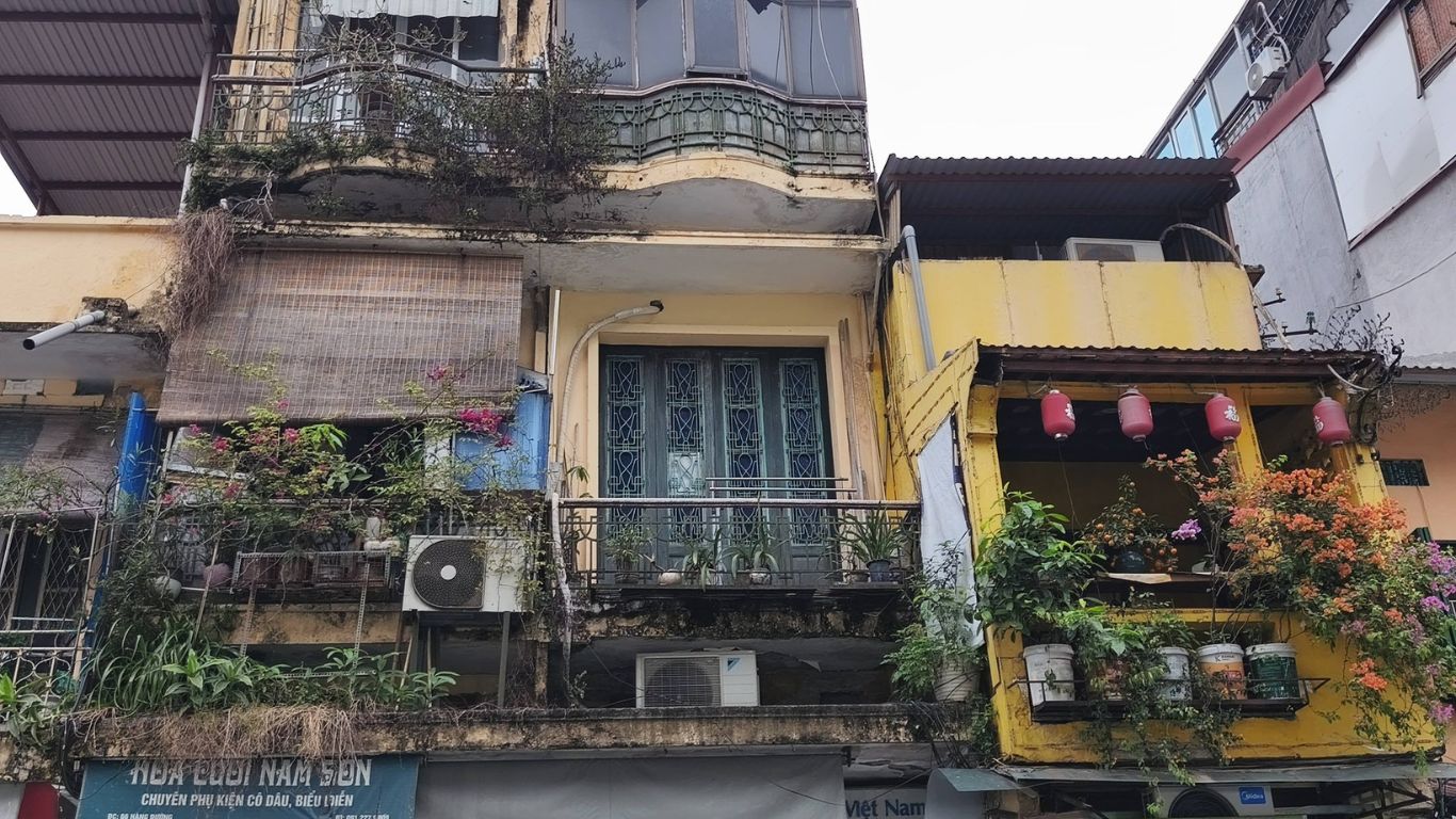 Historic tube houses with balcony plants and lanterns on a narrow street in the Old Quarter of Hanoi