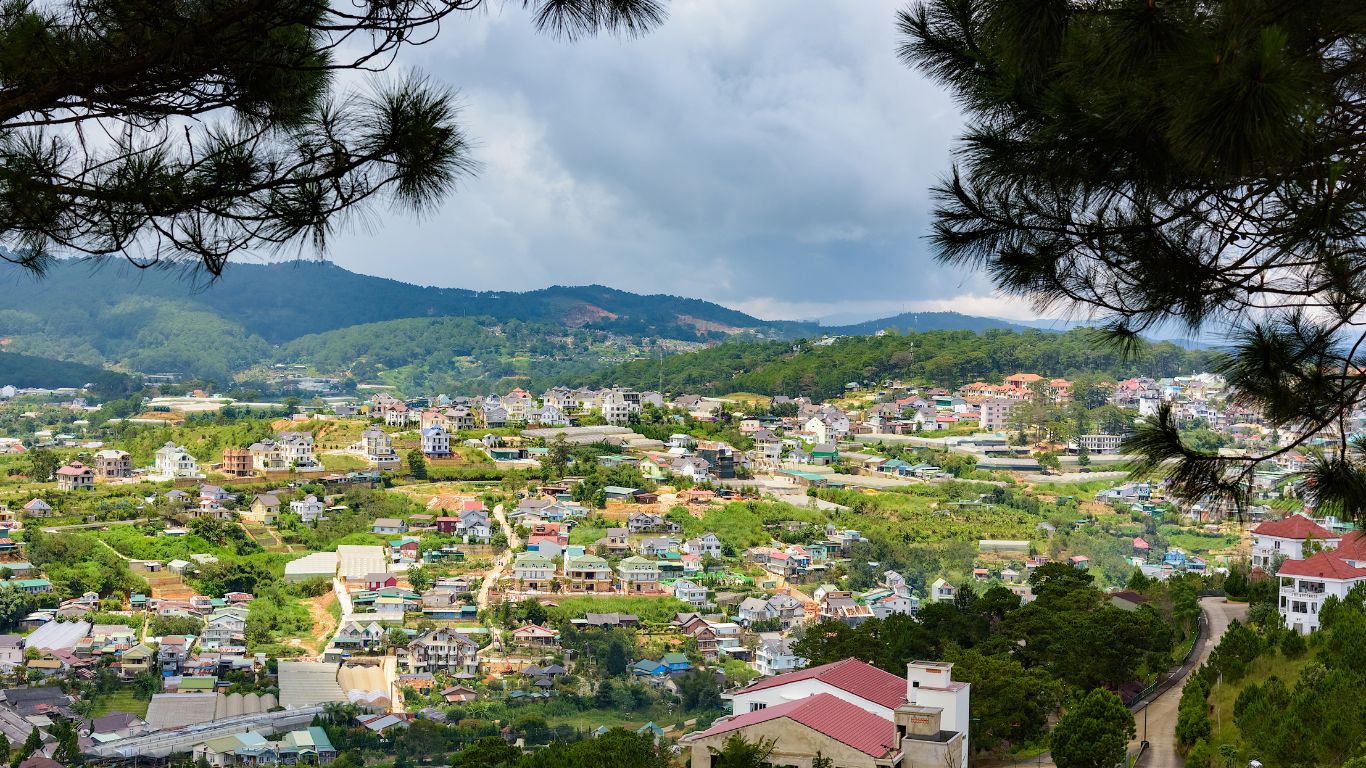 Panoramic view of Da Lat city with houses scattered among green hills and pine trees under a cloudy sky in Vietnam.