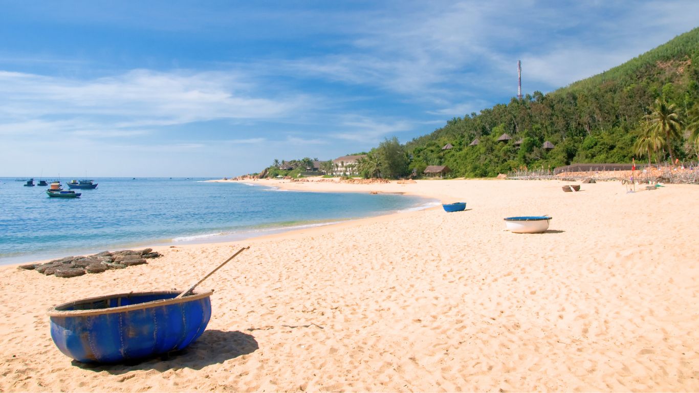 Quy Nhon beach in Vietnam with golden sand clear blue water and traditional basket boats along a quiet shoreline