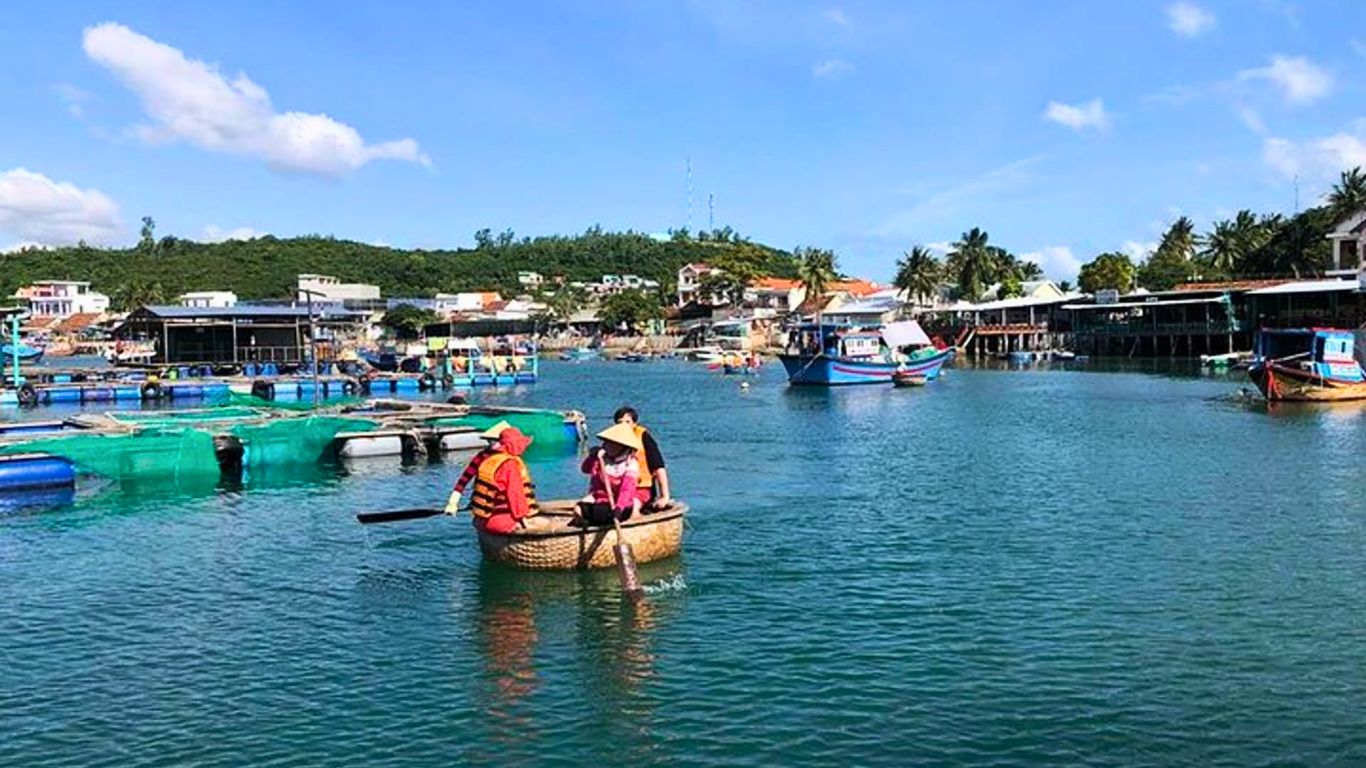 Tourists riding a traditional basket boat in a fishing village in Nha Trang, Vietnam with floating fish farms and coastal houses.
