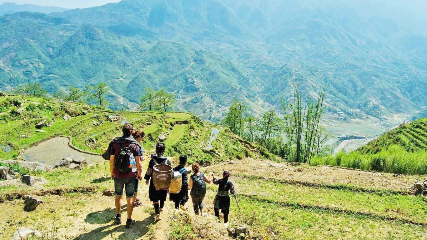 Trekkers walking with Hmong local guides through green rice terrace valleys in Sapa