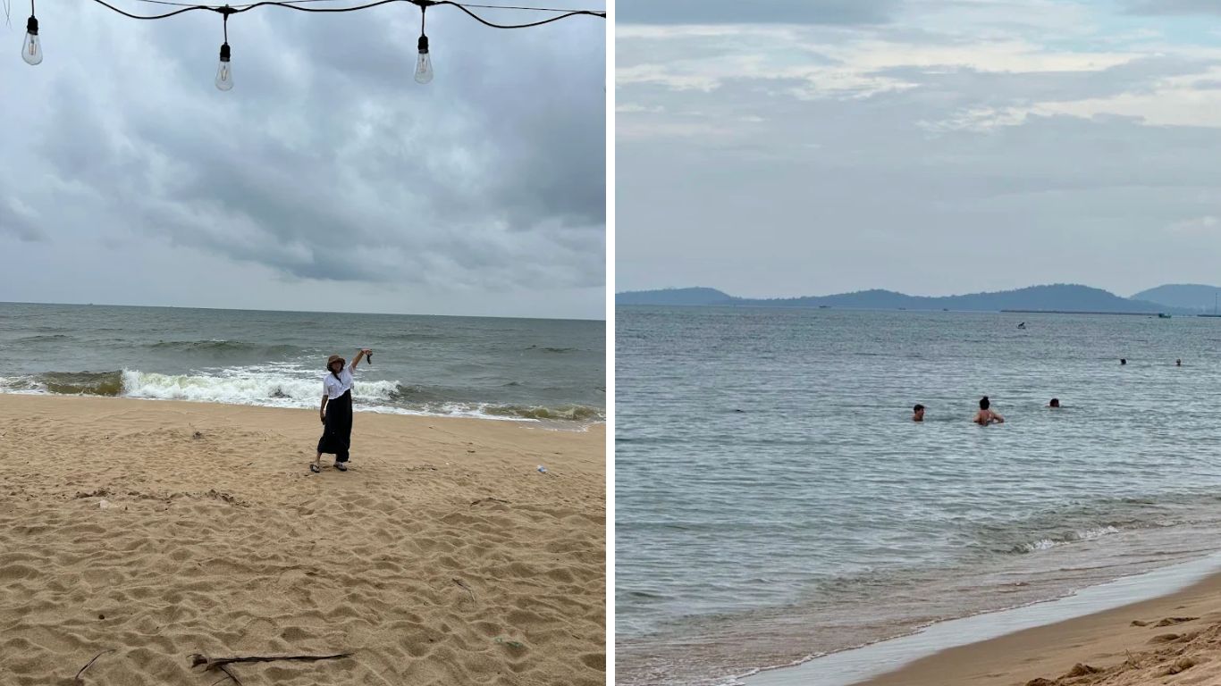 Traveler on a sandy beach in Phu Quoc under a cloudy green season sky, with swimmers enjoying the sea in the background and distant island hills visible on the horizon