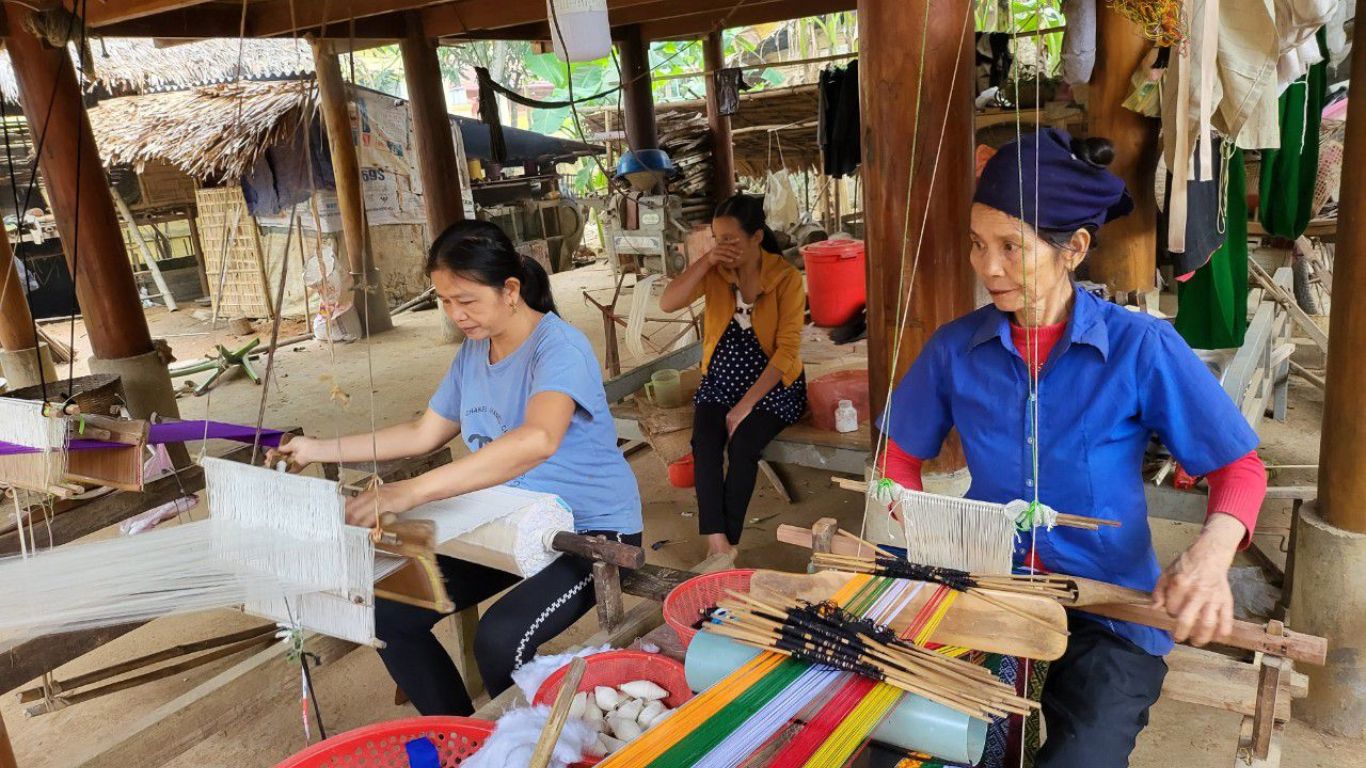Thai ethnic women weaving traditional fabric on wooden looms inside a stilt house village in Pu Luong Nature Reserve.