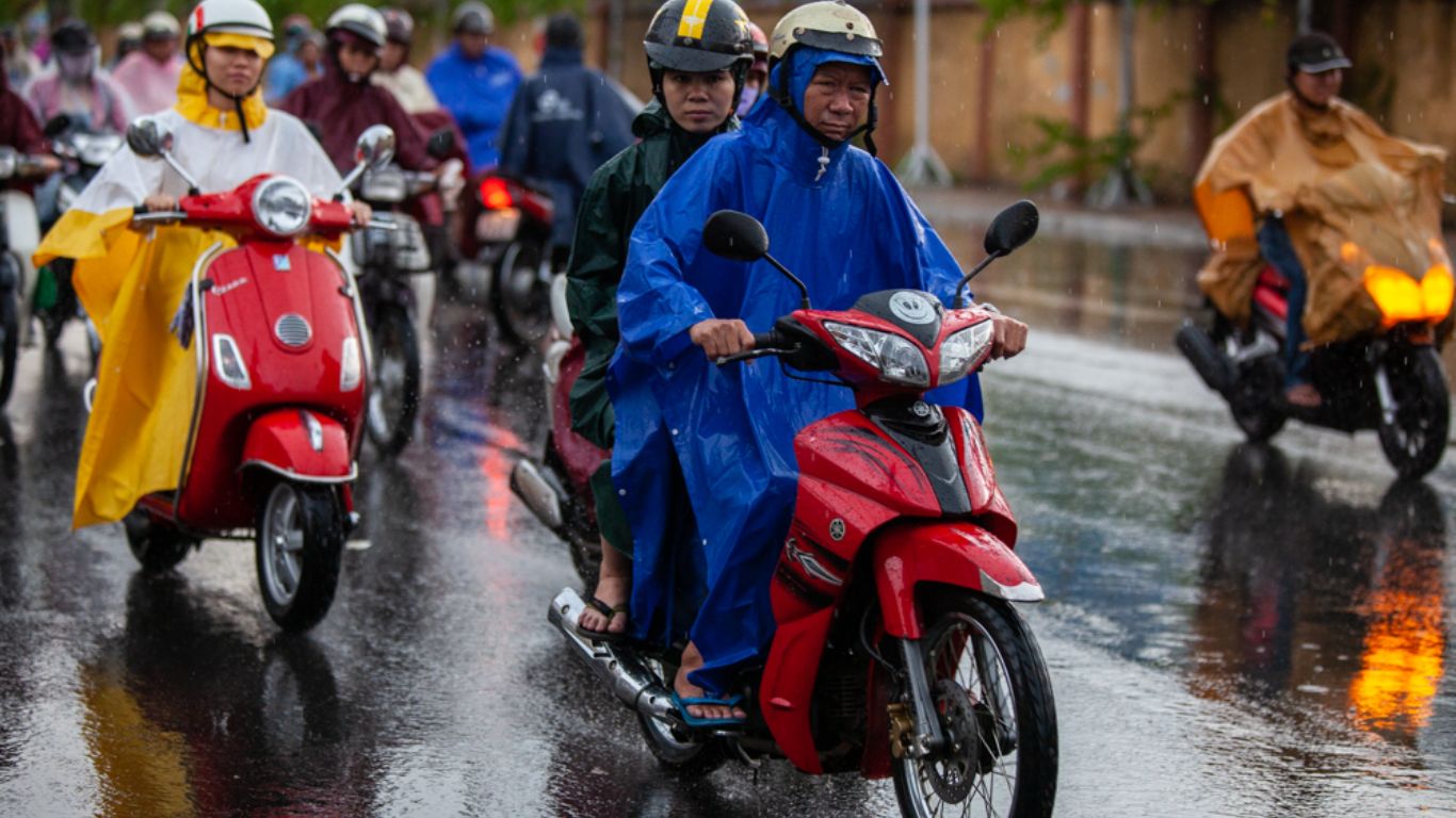 Motorbike riders wearing rain ponchos riding through wet streets in Ho Chi Minh City during June rainy season