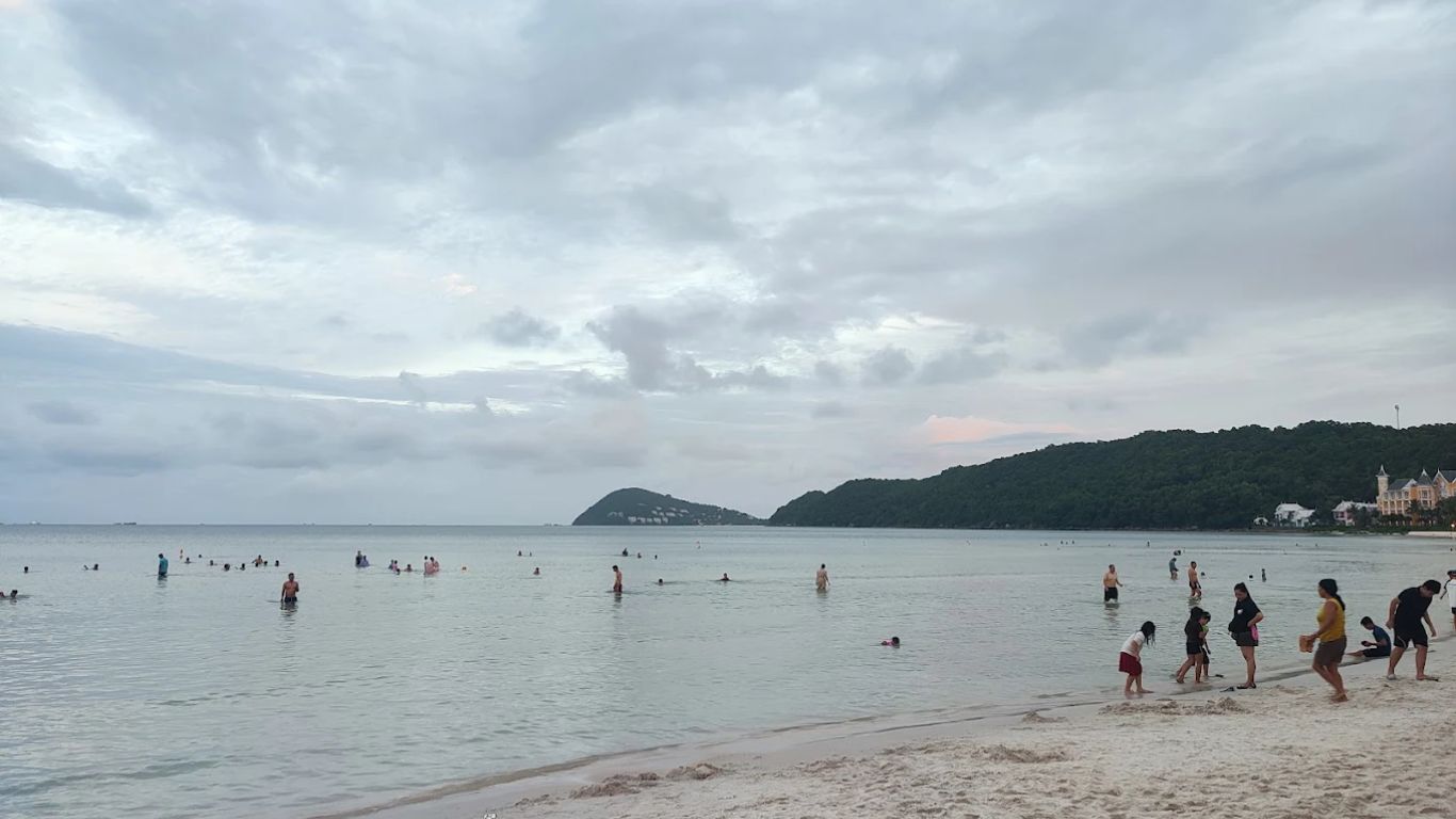 Visitors swimming at a calm sheltered beach in Phu Quoc under cloudy July sky, showing rainy season weather conditions