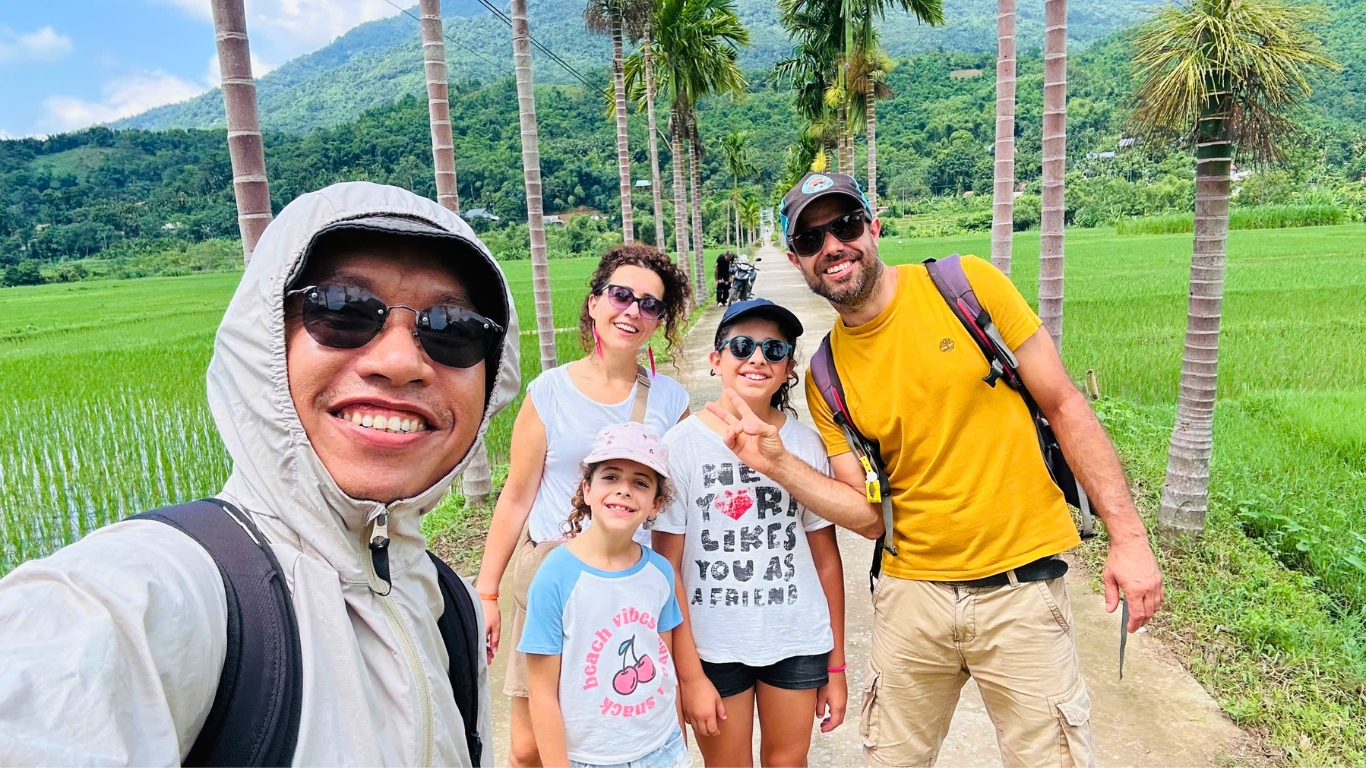 Private tour guide with family walking palm-lined path through Pu Luong rice fields